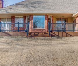 A spacious backyard deck with stairs and railing, providing outdoor living space connected to a brick home. Deck with wooden stairs and railing overlooking a sloped yard, attached to a brick house.