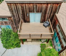 default Aerial view of a wooden deck attached to a rustic house with outdoor seating and lush greenery.