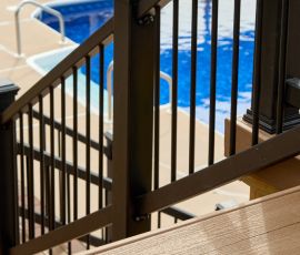 Durable wooden deck railing with black metal balusters near a swimming pool for safety and style. Custom wooden deck railing overlooking a backyard pool area.