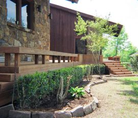 Beautiful outdoor wooden deck with stairs, surrounded by greenery and landscaping. Deck with wooden railing and stairs in a lush garden setting.