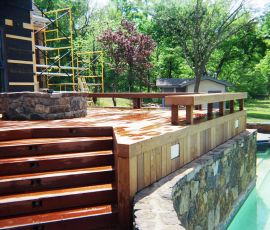 Beautiful backyard with a newly built wooden deck, stone retaining wall, and swimming pool, perfect for outdoor entertainment and relaxation. Custom wooden deck with stone retaining wall and poolside area for outdoor living.