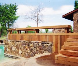 A beautifully crafted outdoor deck featuring a stone foundation, wooden railing, and stairs, perfect for outdoor living and entertaining. Custom outdoor deck with stone foundation and wooden stairs by Deckworks.