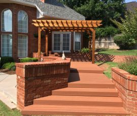 A well-designed wooden deck with a pergola, brick steps, and lush greenery in a suburban backyard setting. Beautiful wooden deck with pergola and brick steps in a residential backyard.