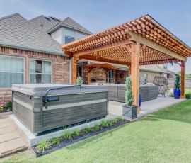 Spacious backyard patio featuring a hot tub, wooden pergola, and comfortable outdoor furniture for relaxing and entertaining. Beautiful backyard patio with hot tub, pergola, and outdoor seating area by Deckworks.