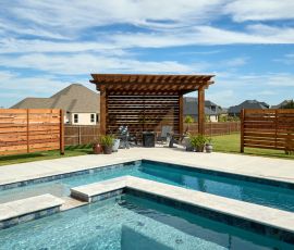 Modern backyard pool with privacy fencing and a shaded seating area for relaxing outdoor gatherings. Custom backyard pool with wooden privacy fences and shaded lounge area.